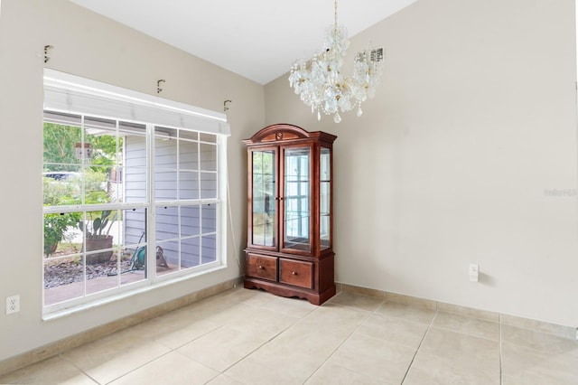 spare room featuring a notable chandelier, light tile floors, and lofted ceiling