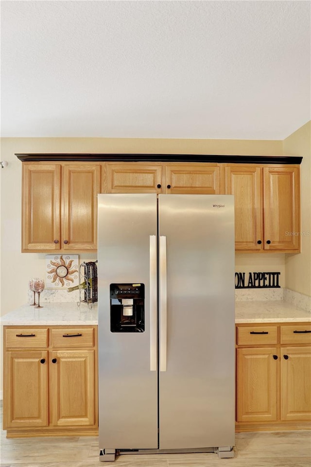 kitchen with light stone countertops, stainless steel fridge, light hardwood / wood-style flooring, and light brown cabinetry