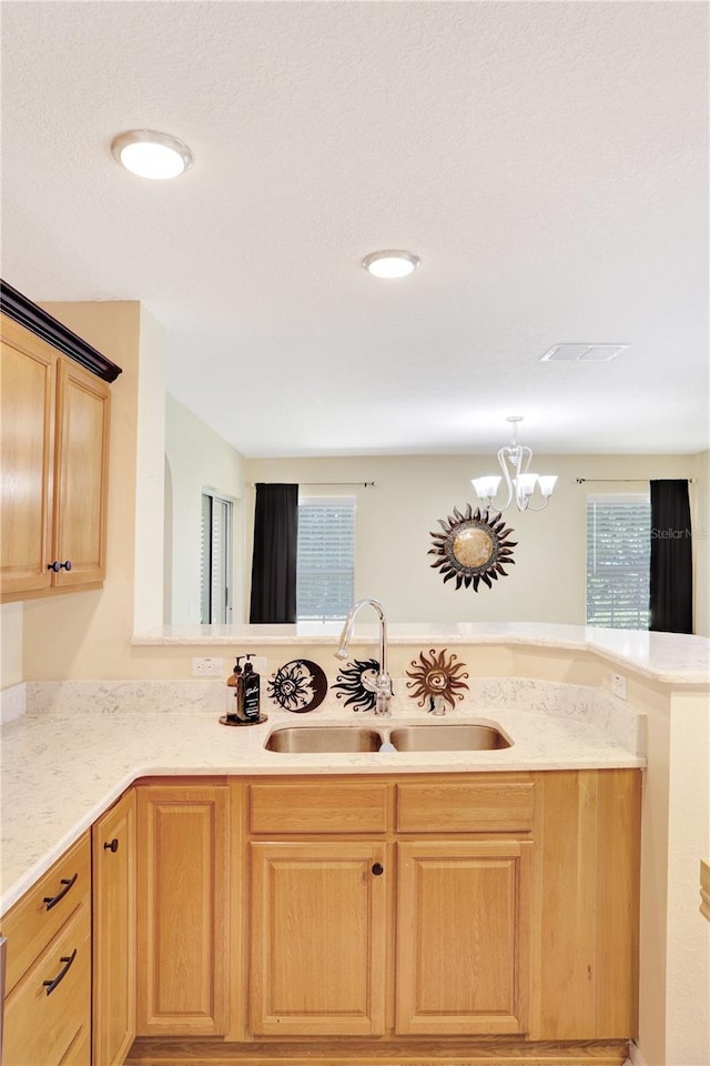 kitchen with a healthy amount of sunlight, an inviting chandelier, sink, and kitchen peninsula