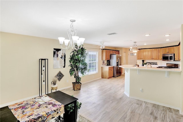 kitchen featuring ceiling fan with notable chandelier, stainless steel appliances, a kitchen bar, light wood-type flooring, and pendant lighting