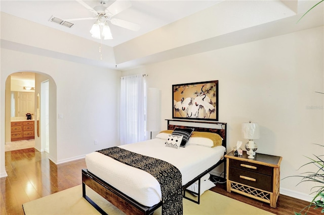 bedroom featuring ceiling fan, a tray ceiling, connected bathroom, and wood-type flooring