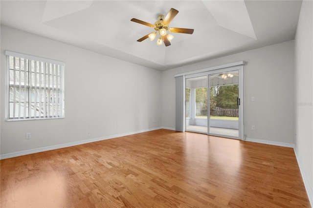 unfurnished room with light wood-type flooring, ceiling fan, and a raised ceiling