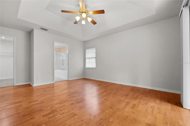 unfurnished bedroom with ensuite bath, light hardwood / wood-style flooring, ceiling fan, and a raised ceiling