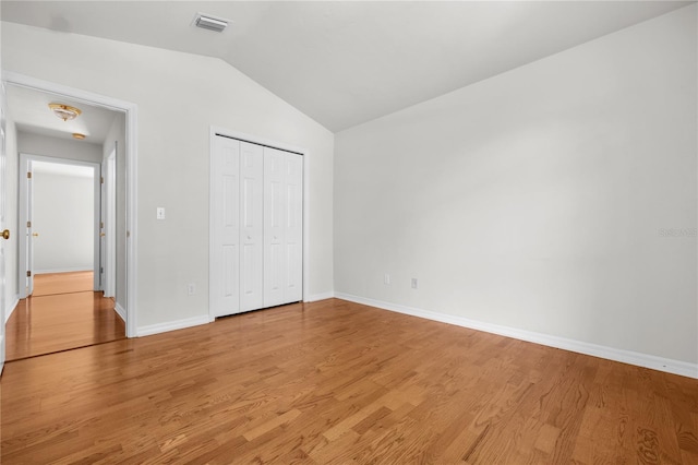 unfurnished bedroom featuring light wood-type flooring, lofted ceiling, and a closet