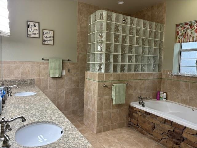 bathroom with tiled bath, dual vanity, tile flooring, and tile walls