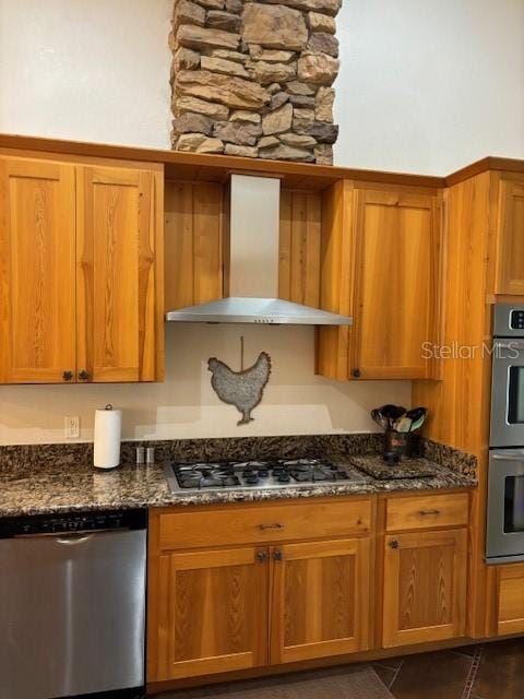 kitchen with appliances with stainless steel finishes, dark stone counters, and wall chimney exhaust hood