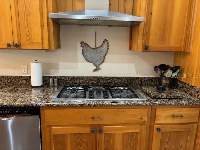 kitchen with stainless steel appliances, dark stone counters, and wall chimney exhaust hood