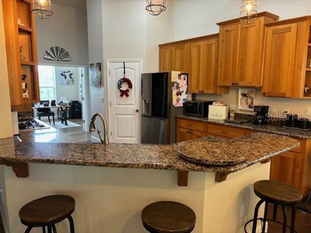 kitchen with decorative light fixtures, a breakfast bar area, kitchen peninsula, and fridge with ice dispenser