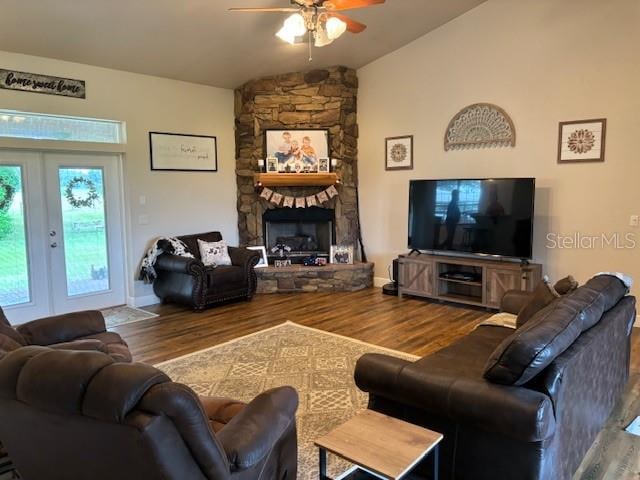 living room with ceiling fan, hardwood / wood-style flooring, a stone fireplace, french doors, and lofted ceiling