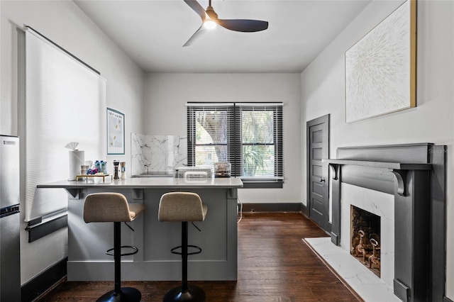 kitchen with a kitchen breakfast bar, ceiling fan, dark hardwood / wood-style flooring, and a premium fireplace