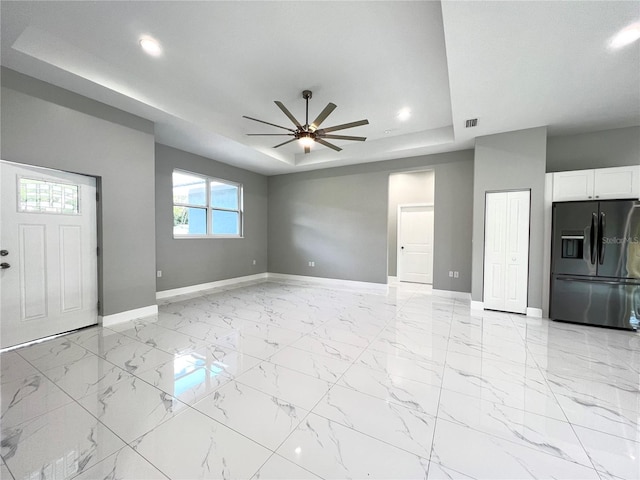 unfurnished living room featuring ceiling fan, a raised ceiling, and light tile flooring