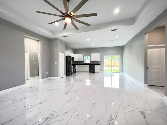 unfurnished living room with a tray ceiling, ceiling fan, and light tile flooring