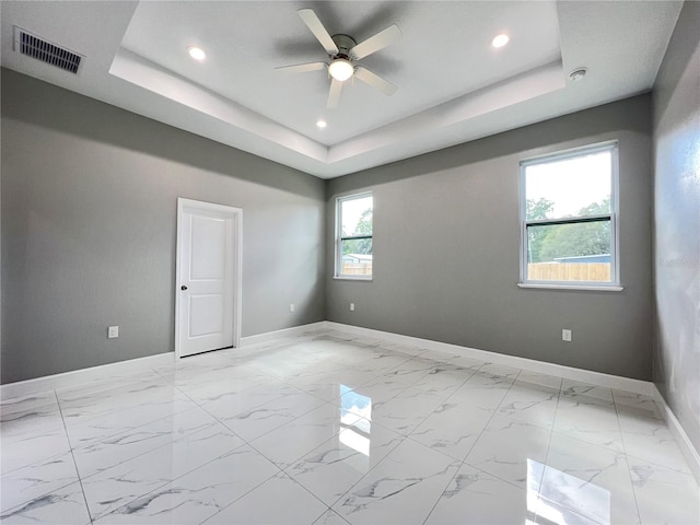 tiled empty room featuring ceiling fan and a raised ceiling