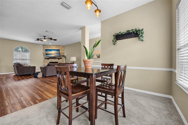 carpeted dining room with ceiling fan with notable chandelier and a stone fireplace