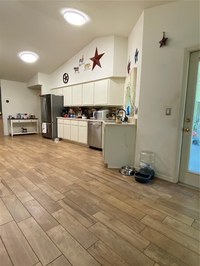 kitchen featuring stainless steel appliances, vaulted ceiling, sink, light hardwood / wood-style floors, and white cabinetry