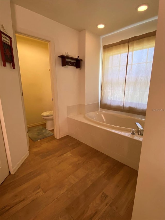 bathroom with hardwood / wood-style floors, toilet, and tiled tub