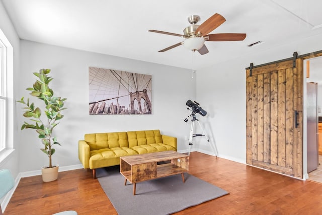 living room with wood-type flooring, a barn door, and ceiling fan