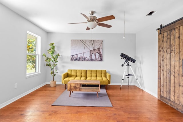 living area featuring a barn door, ceiling fan, and hardwood / wood-style flooring