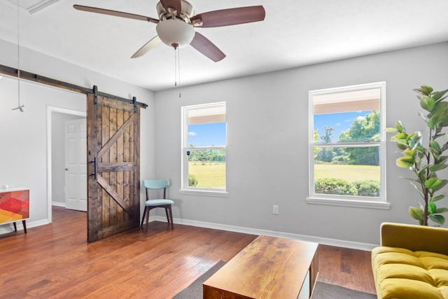 sitting room with a barn door, ceiling fan, a healthy amount of sunlight, and wood-type flooring