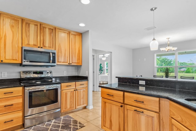 kitchen with pendant lighting, ceiling fan with notable chandelier, dark stone countertops, appliances with stainless steel finishes, and light tile patterned flooring