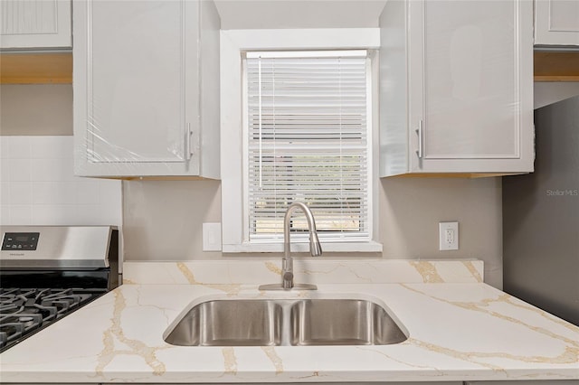 kitchen featuring light stone counters, sink, stainless steel gas stove, and white cabinets