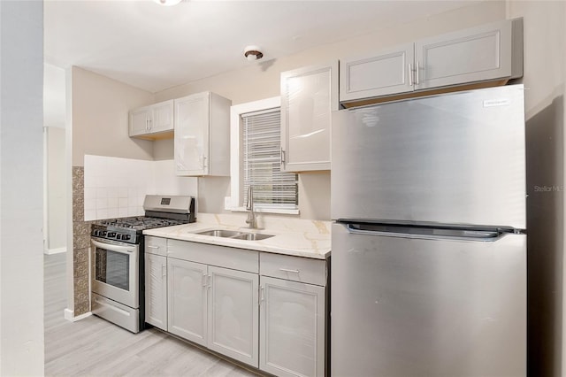 kitchen featuring appliances with stainless steel finishes, sink, decorative backsplash, light hardwood / wood-style floors, and light stone countertops