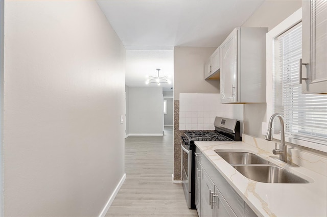 kitchen with sink, white cabinetry, light stone counters, stainless steel range with gas stovetop, and backsplash