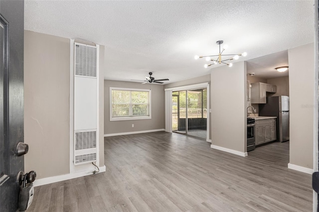 unfurnished living room with sink, ceiling fan with notable chandelier, a textured ceiling, and light wood-type flooring