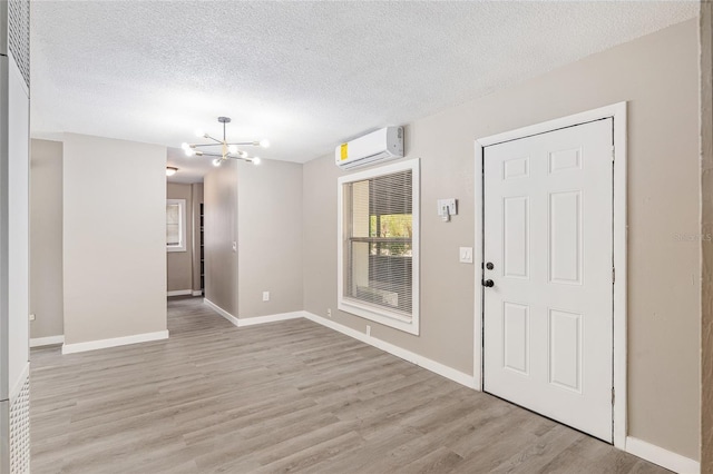 foyer with an inviting chandelier, light hardwood / wood-style floors, a textured ceiling, and an AC wall unit