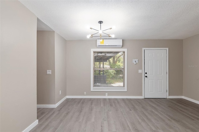 interior space with a notable chandelier, a textured ceiling, a wall unit AC, and light hardwood / wood-style flooring