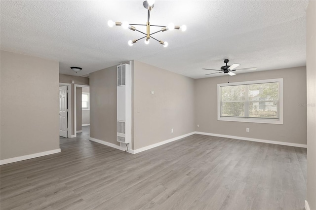 spare room featuring wood-type flooring, ceiling fan with notable chandelier, and a textured ceiling