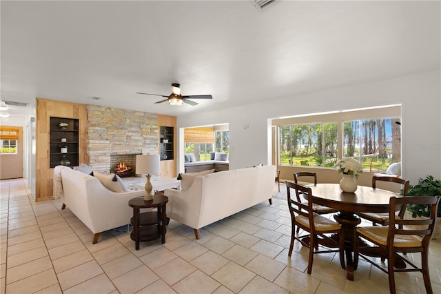 living room featuring built in features, a stone fireplace, ceiling fan, and light tile floors