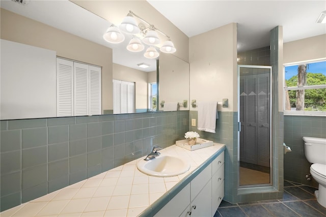 bathroom with tile patterned flooring, toilet, tile walls, vanity, and a chandelier