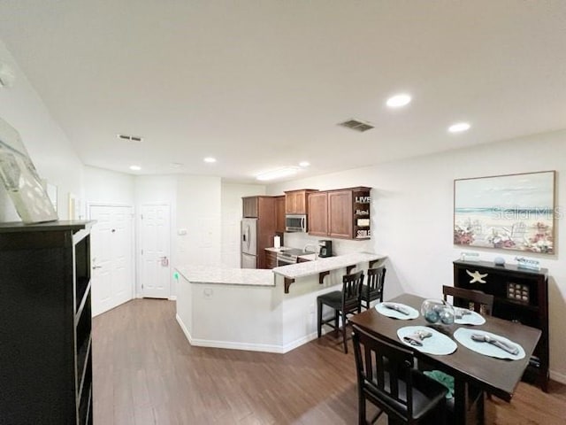 kitchen featuring appliances with stainless steel finishes, dark hardwood / wood-style flooring, kitchen peninsula, and a breakfast bar area