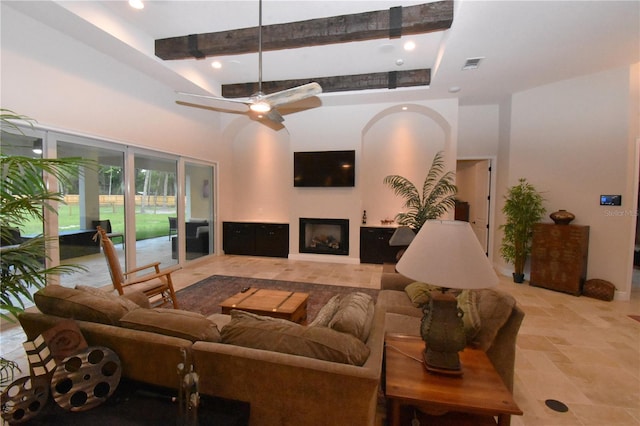 living room with ceiling fan, beam ceiling, and a towering ceiling