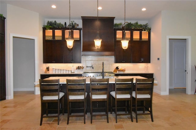 kitchen with pendant lighting, backsplash, a kitchen breakfast bar, dark brown cabinetry, and a center island with sink