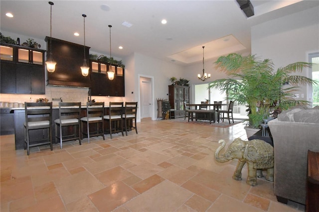 kitchen with a kitchen island, a breakfast bar area, hanging light fixtures, a raised ceiling, and an inviting chandelier