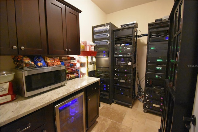 kitchen featuring wine cooler, light stone counters, and dark brown cabinets