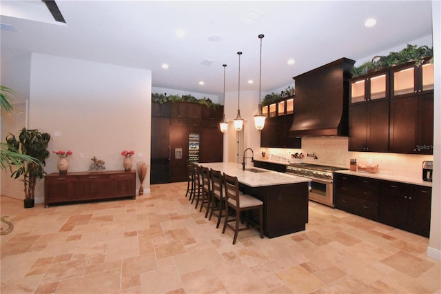 kitchen featuring hanging light fixtures, double oven range, a kitchen breakfast bar, custom range hood, and a kitchen island with sink