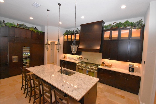 kitchen featuring sink, custom exhaust hood, hanging light fixtures, a center island with sink, and decorative backsplash