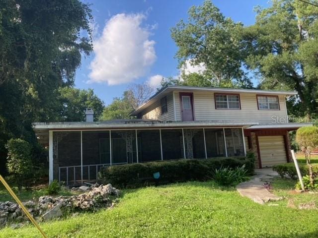 back of property with a sunroom, a yard, and a garage