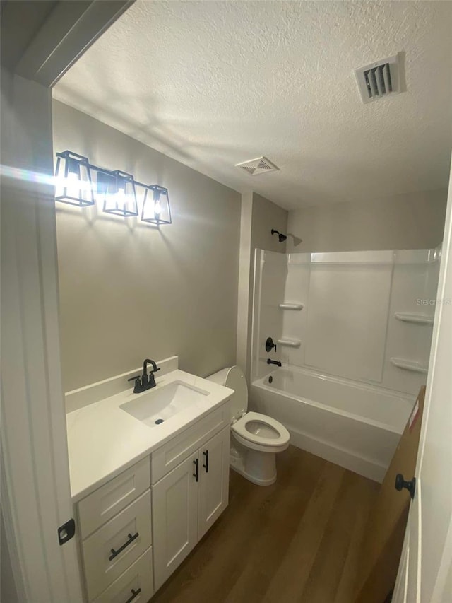 full bathroom with vanity, a textured ceiling, shower / washtub combination, wood-type flooring, and toilet