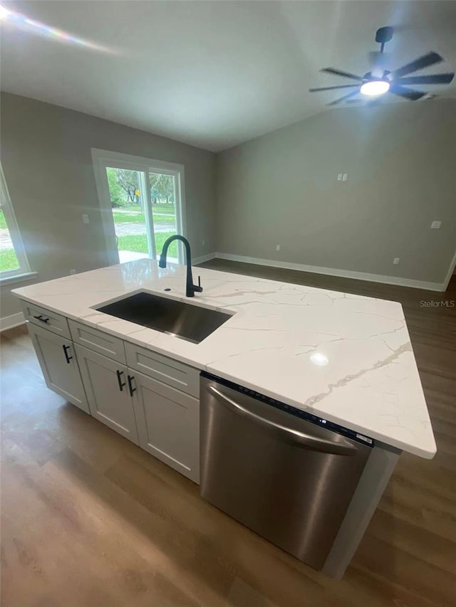 kitchen with light stone counters, stainless steel dishwasher, a kitchen island with sink, sink, and white cabinetry