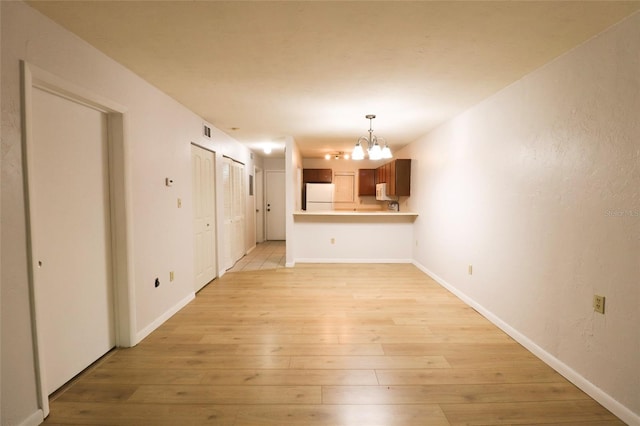 unfurnished living room with light wood-type flooring and an inviting chandelier