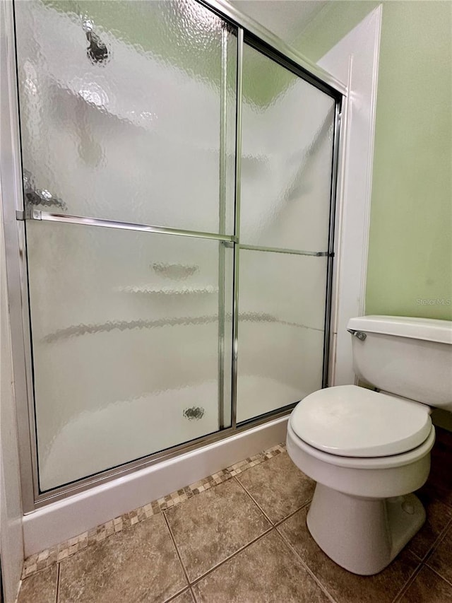 bathroom featuring toilet, an enclosed shower, and tile patterned flooring