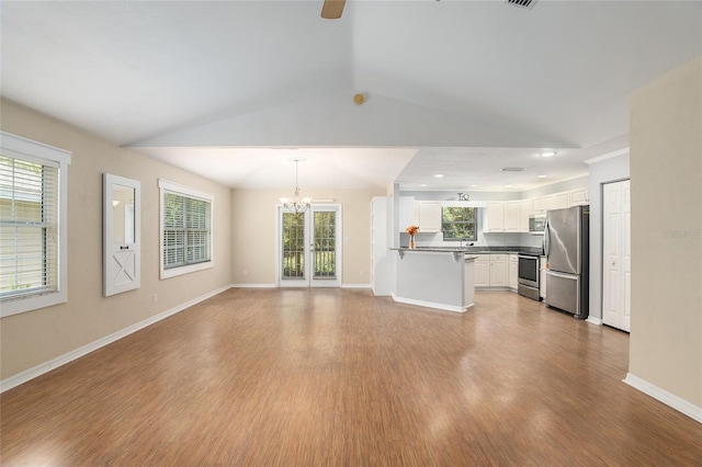 unfurnished living room with ceiling fan with notable chandelier, light hardwood / wood-style floors, and vaulted ceiling