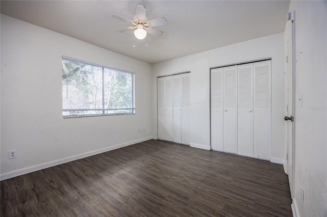 unfurnished bedroom with ceiling fan, dark wood-type flooring, and two closets