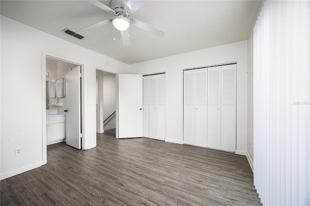 unfurnished bedroom featuring connected bathroom, ceiling fan, multiple closets, and dark wood-type flooring