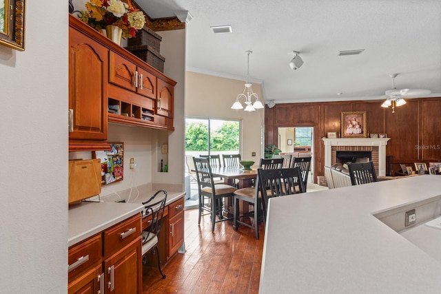 kitchen featuring dark hardwood / wood-style floors, pendant lighting, a fireplace, ceiling fan with notable chandelier, and ornamental molding