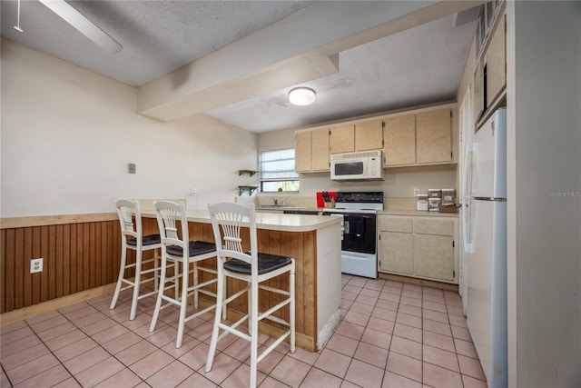 kitchen featuring kitchen peninsula, a textured ceiling, white appliances, a breakfast bar area, and wooden walls